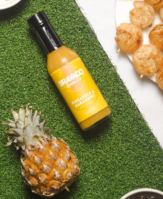 Bravado Spice Pineapple & Habanero hot sauce with a fresh pineapple and grilled shrimp beside it.