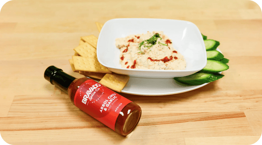 smoked salmon dip in a bowl with crackers and cucumbers, bottle of Arbol Chili & Garlic Hot Sauce
